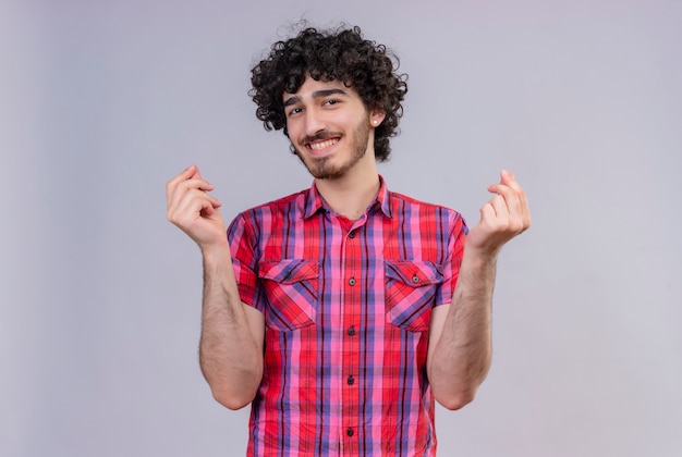 Un heureux jeune bel homme aux cheveux bouclés en chemise à carreaux montrant le geste de l'argent