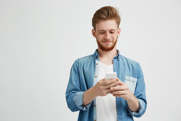 Heureux jeune bel homme souriant regardant téléphone surfer sur Internet, surfer sur le Web.