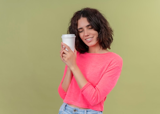 Heureux jeune belle femme tenant une tasse de café en plastique sur un mur vert isolé avec espace copie