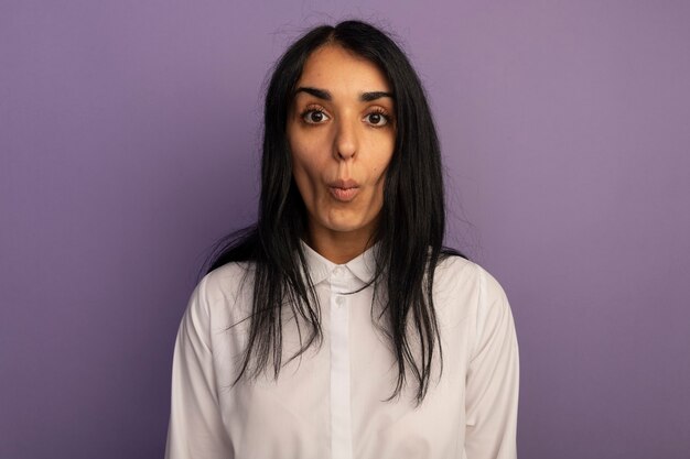 Heureux jeune belle fille regardant droit devant portant un t-shirt blanc montrant le geste de baiser isolé sur violet