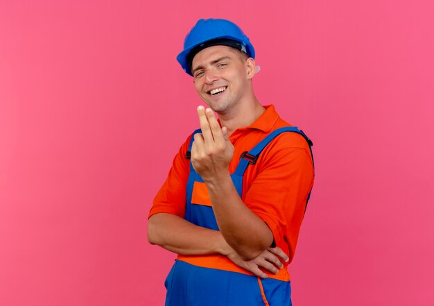 Heureux jeune constructeur masculin portant l'uniforme et un casque de sécurité montrant deux sur rose