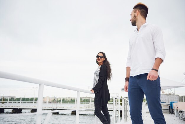 Heureux jeune couple amoureux dans une belle robe, posant sur la jetée près de l'eau.