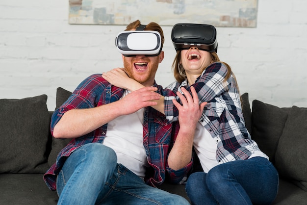 Heureux jeune couple assis sur un canapé avec un casque vr et faisant l&#39;expérience de la réalité virtuelle