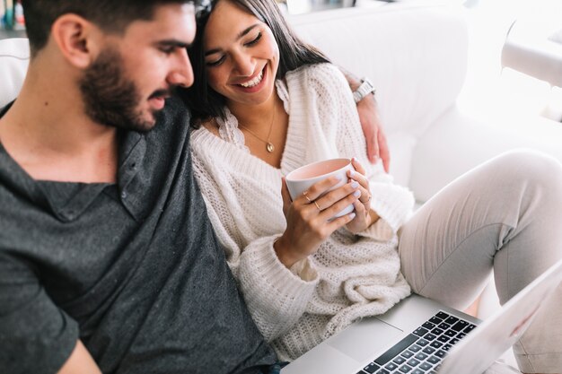 Heureux jeune couple assis sur un canapé avec un ordinateur portable