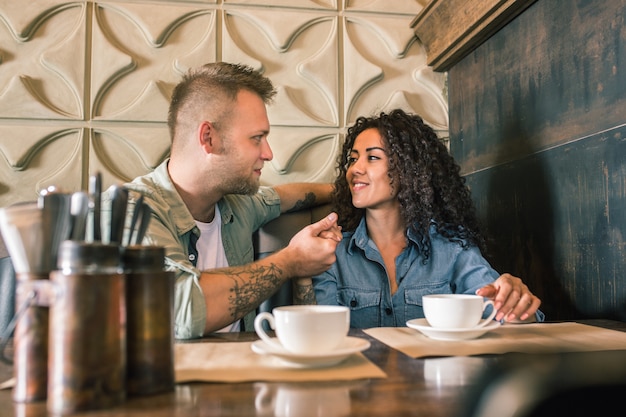 Heureux jeune couple boit du café et souriant tout en étant assis au café