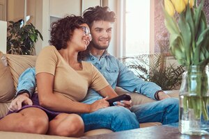 Photo gratuite heureux jeune couple câlins tout en regardant la télévision dans leur salon.
