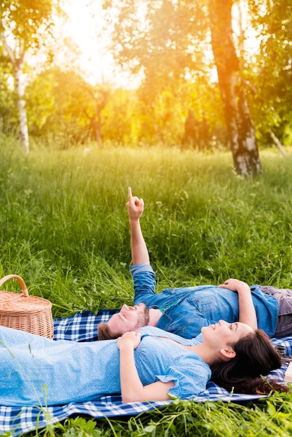 Heureux jeune couple cherche ciel en position couchée sur une couverture dans la nature