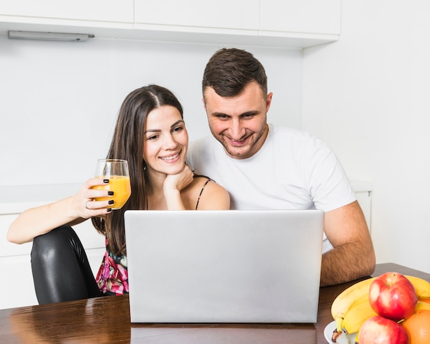 Heureux jeune couple cherche un ordinateur portable dans la cuisine