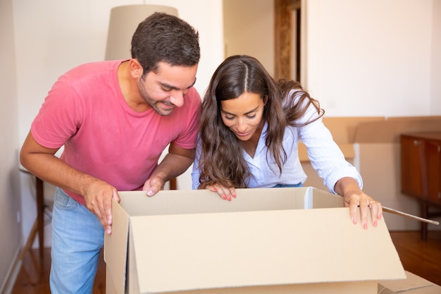 Heureux jeune couple latin excité ouvrant la boîte de carton et regardant à l'intérieur, déplacer et déballer des choses