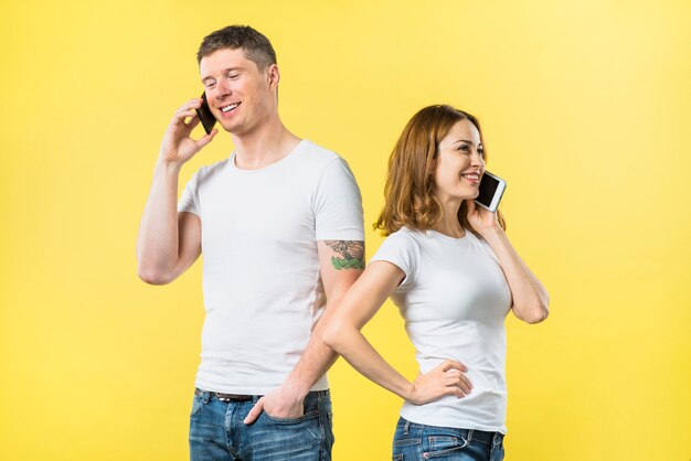 Heureux jeune couple parlant au téléphone portable debout sur fond jaune