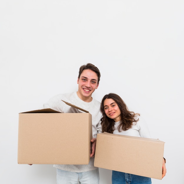 Heureux jeune couple portant des boîtes en carton dans la main en regardant la caméra isolé sur fond blanc