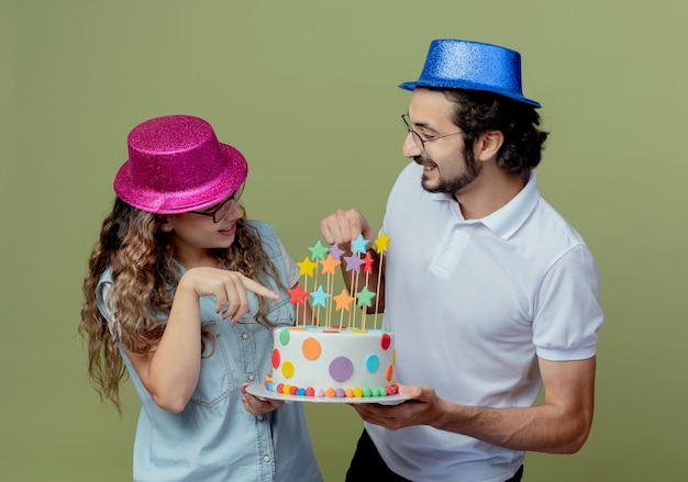 Heureux jeune couple portant un chapeau rose et bleu se regardent et pointe le gâteau d'anniversaire dans la main de l'homme