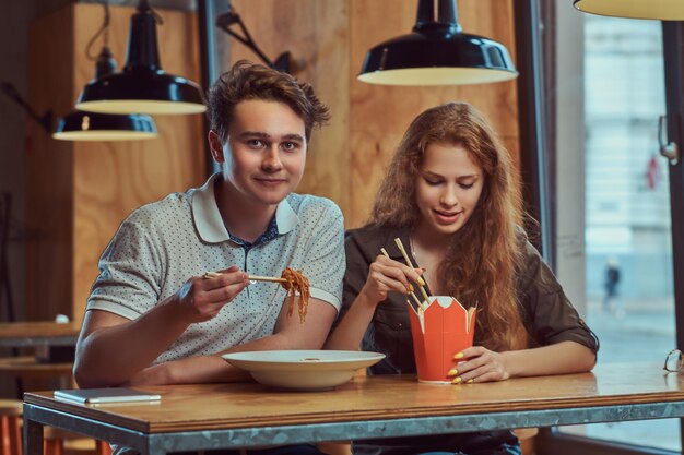 Heureux jeune couple portant des vêtements décontractés mangeant des nouilles épicées dans un restaurant asiatique.