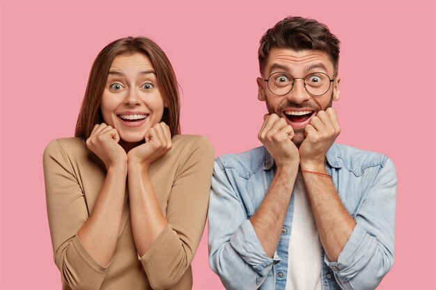 Heureux jeune couple posant contre le mur rose