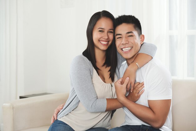 Heureux jeune couple de race mixte étreignant et souriant à la maison