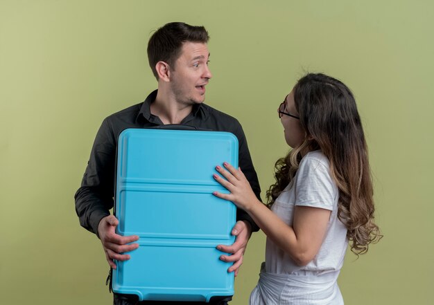 Heureux jeune couple de touristes homme et femme tenant une valise à la surprise debout sur un mur léger