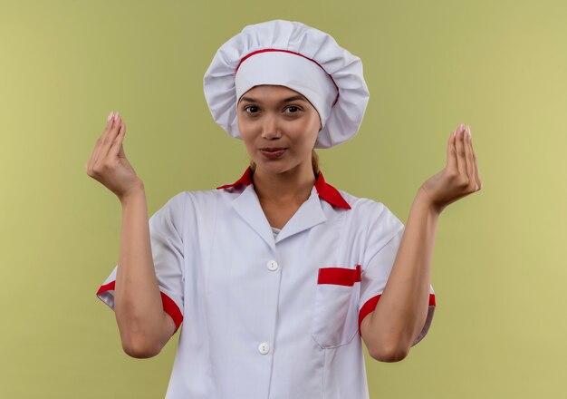 Heureux jeune cuisinier femme portant l'uniforme de chef montrant le geste de pointe sur mur vert isolé