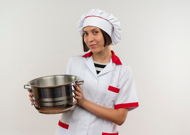 Heureux jeune cuisinier en uniforme de chef holding pot à l'avant isolé sur mur blanc
