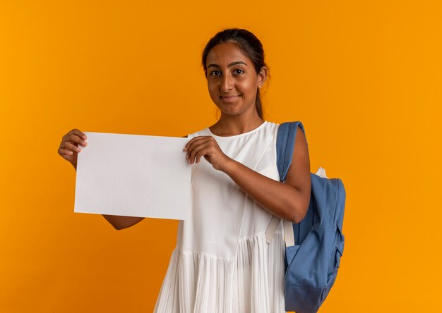 Heureux jeune écolière portant sac à dos tenant du papier sur orange