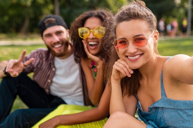 Heureux jeune entreprise élégante et colorée d'amis assis dans le parc, l'homme et la femme s'amusant ensemble