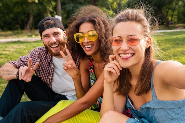 Photo gratuite heureux jeune entreprise élégante et colorée d'amis assis dans le parc, l'homme et la femme s'amusant ensemble