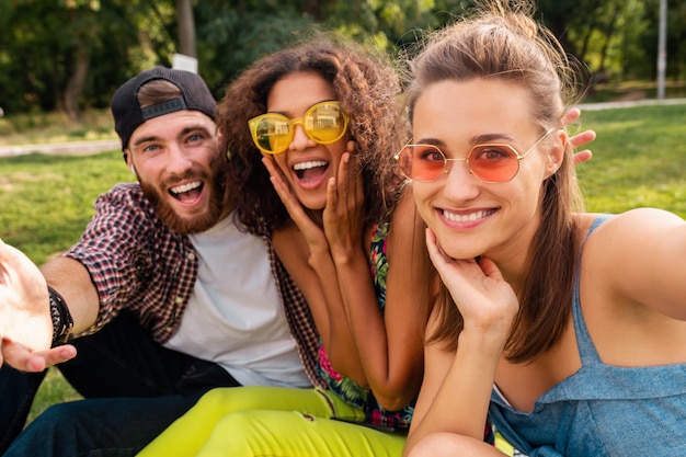 Heureux jeune entreprise élégante et colorée d'amis assis dans le parc, l'homme et la femme s'amusant ensemble