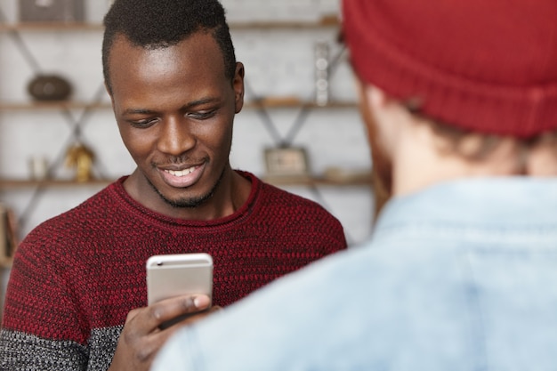 Heureux jeune étudiant afro-américain portant un chandail tenant un téléphone mobile générique