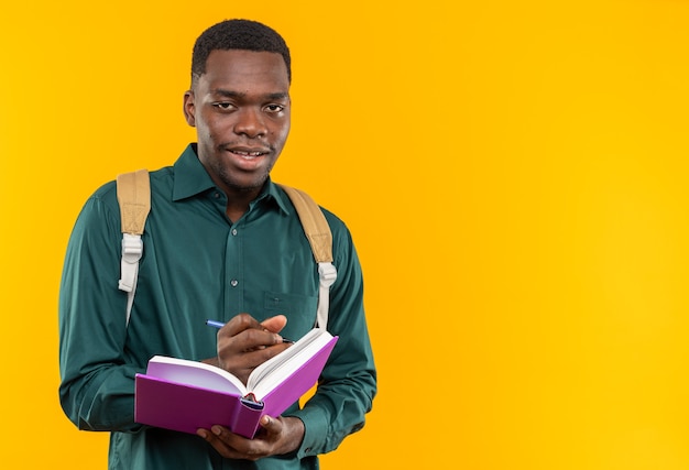 Heureux jeune étudiant afro-américain avec sac à dos tenant un livre et un crayon