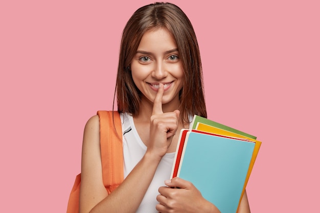 Heureux jeune étudiant posant contre le mur rose