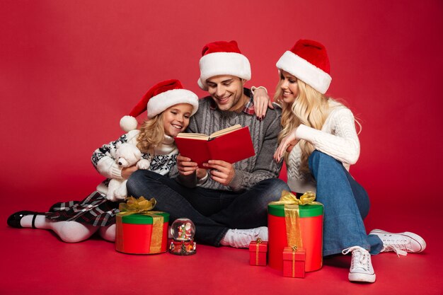 Heureux jeune famille portant des chapeaux de Noël assis isolé