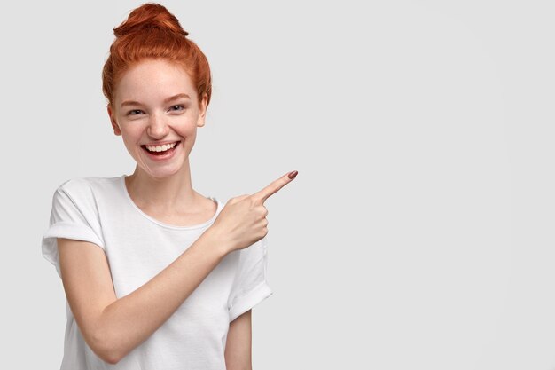 Heureux jeune femme aux cheveux roux avec un sourire charmant, montre de l'espace libre, annonce quelque chose