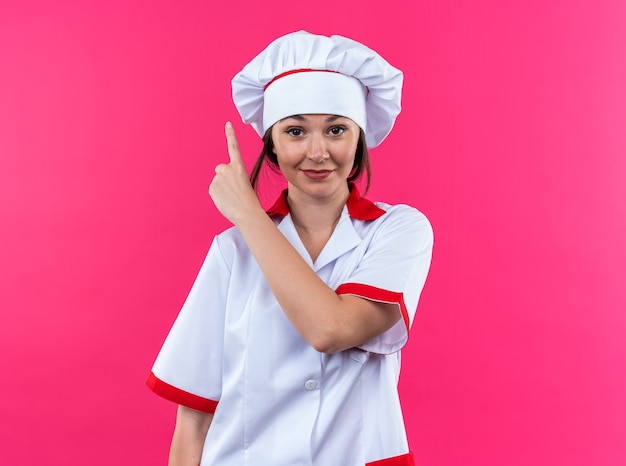 Heureux jeune femme cuisinier portant des points uniformes de chef à haut isolé sur fond rose