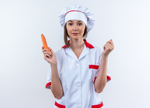 Heureux jeune femme cuisinier portant l'uniforme de chef holding carotte isolé sur fond blanc