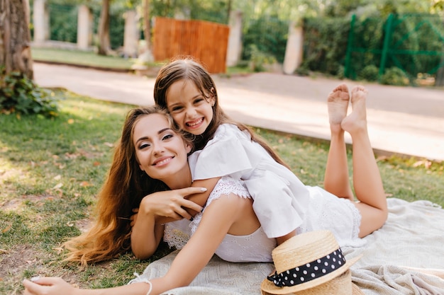 Heureux jeune femme avec un maquillage éclatant se détendre sur une couverture avec les jambes et souriant. Rire fille bronzée couchée sur le dos de la mère