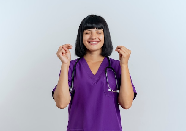 Heureux jeune femme médecin brune en uniforme avec stéthoscope croise les doigts