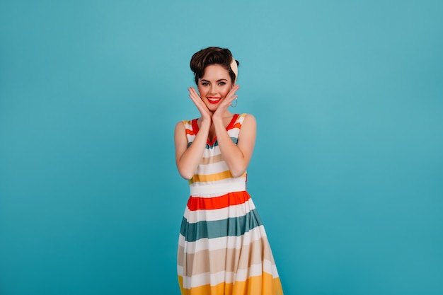 Photo gratuite heureux jeune femme en robe lumineuse touchant le visage. photo de studio de charmante pin-up avec une coiffure élégante.