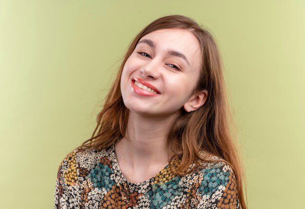 Heureux jeune fille aux cheveux longs portant une robe colorée regardant la caméra positive et sourire heureux