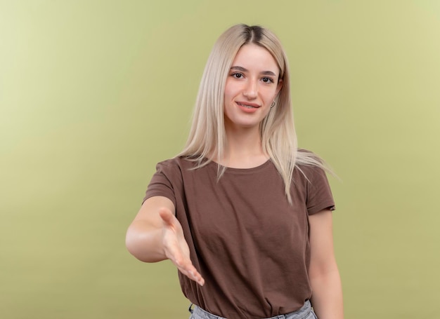 Heureux jeune fille blonde dans un appareil dentaire qui s'étend de la main faisant des gestes salut sur un espace vert isolé avec copie espace