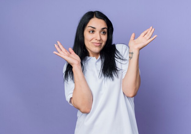 Heureux jeune fille caucasienne brune lève les mains en regardant côté isolé sur mur violet