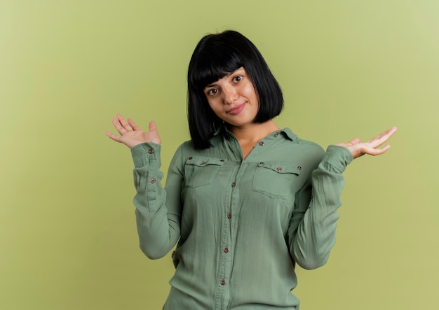 Heureux jeune fille caucasienne brune se tient avec les mains ouvertes isolé sur fond vert olive avec espace copie