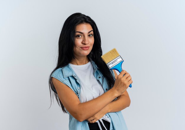 Heureux jeune fille caucasienne se tient avec les bras croisés et tient le pinceau