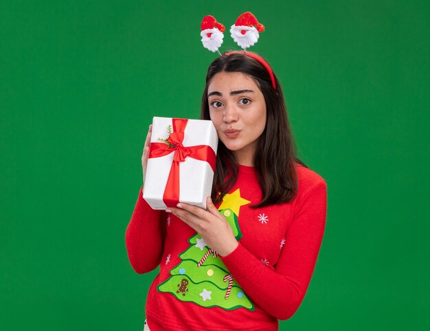 Heureux jeune fille de race blanche avec bandeau de père Noël détient boîte-cadeau de Noël isolé sur fond vert avec espace copie