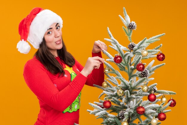 Photo gratuite heureux jeune fille de race blanche avec bonnet de noel sort la langue