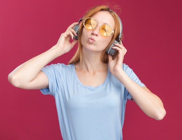 Heureux jeune fille rousse au gingembre avec des taches de rousseur dans des lunettes de soleil et sur un casque debout avec les yeux fermés sur rose