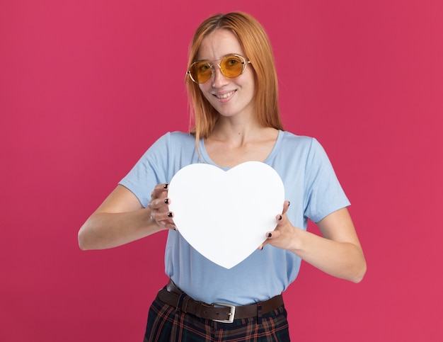 Heureux Jeune Fille Rousse Au Gingembre Avec Des Taches De Rousseur Dans Des Lunettes De Soleil Tient En Forme De Coeur Sur Rose