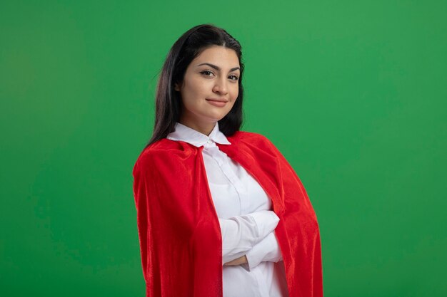 Heureux jeune fille de super-héros caucasien debout avec une posture fermée et souriant isolé sur un mur vert avec espace copie