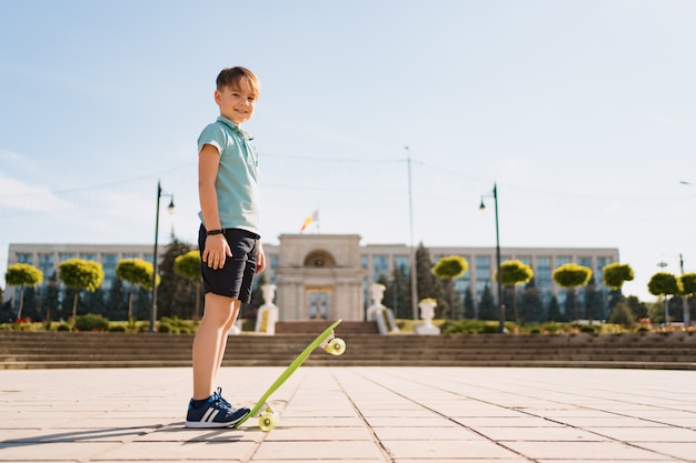 Heureux jeune garçon jouant sur la planche à roulettes dans le parc, enfant de race blanche équitation penny board, pratiquant la planche à roulettes.