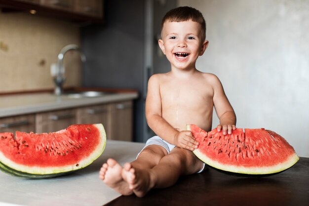 Heureux jeune garçon avec des tranches de melon d'eau