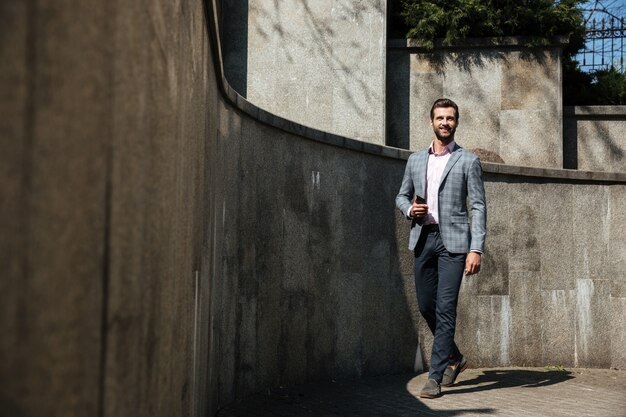 Heureux jeune homme d'affaires marchant à l'extérieur tenant le téléphone