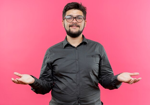 Heureux jeune homme d'affaires portant des lunettes se propage les mains isolés sur un mur rose